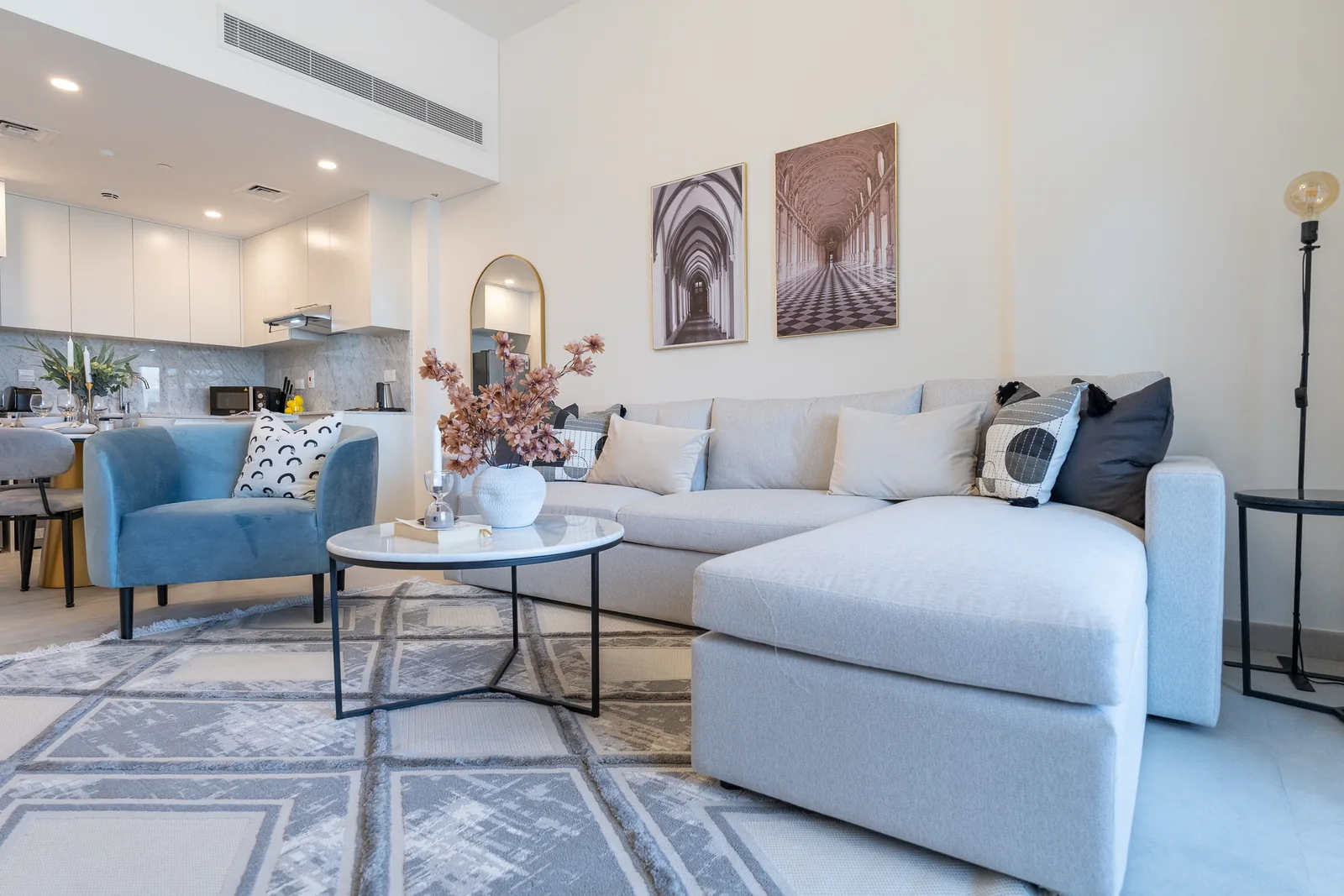 Pale sectional sofa, blue chair and round coffee table with an open kitchen behind.