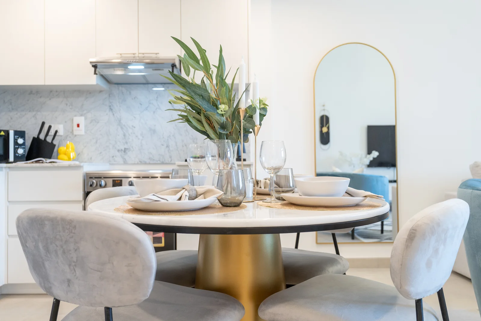 Round dining table on a gold-toned base with upholstered chairs and place settings.