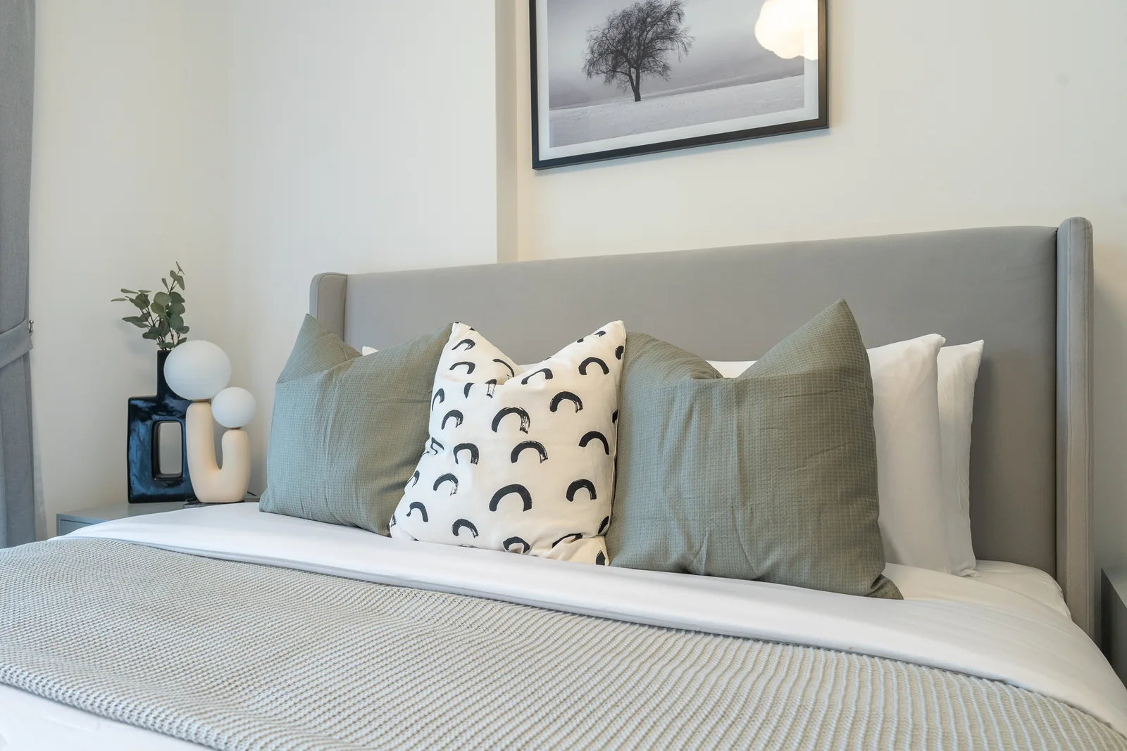Grey upholstered headboard with green and patterned cushions.