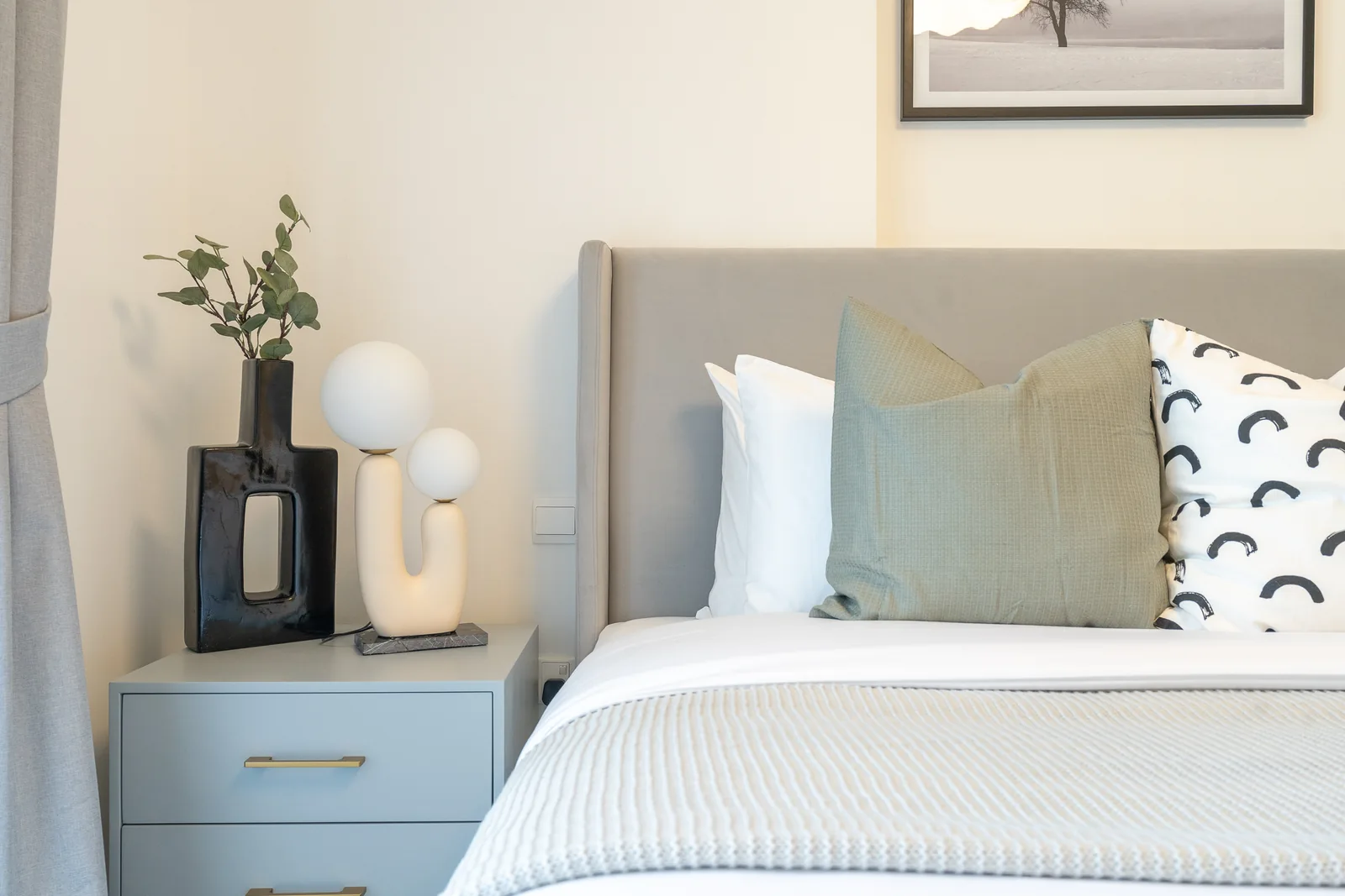 Pale grey bedside cabinet with a globe lamp and vase beside the bed.