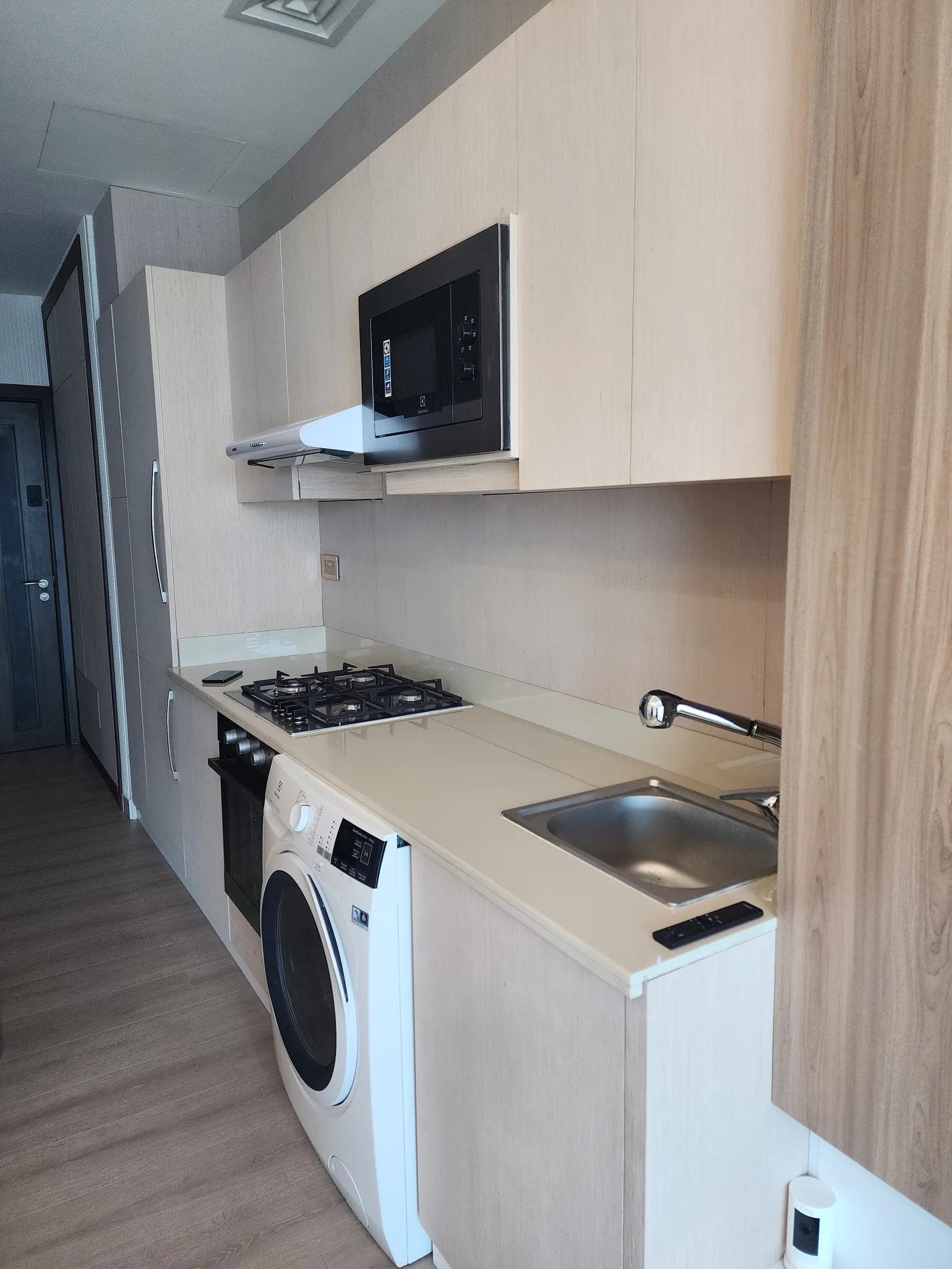 Compact kitchenette with pale cabinetry, a sink and appliances in one run.