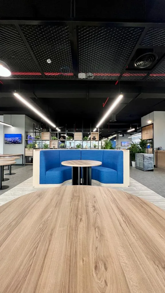 Round timber-toned tabletop facing a curved blue upholstered booth with a pale outer shell.