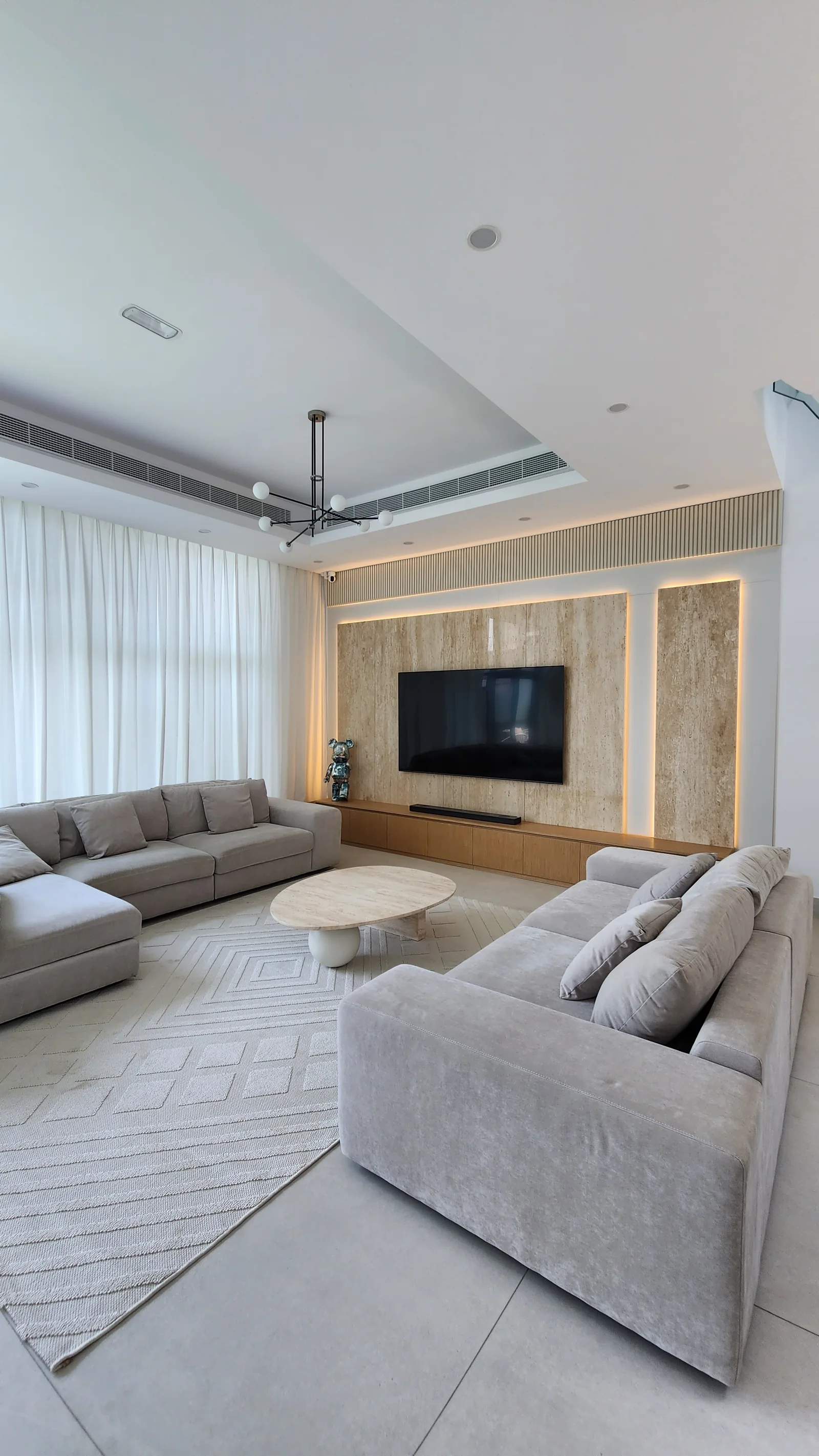 Living-room overview with pale sofas, table and illuminated TV wall.