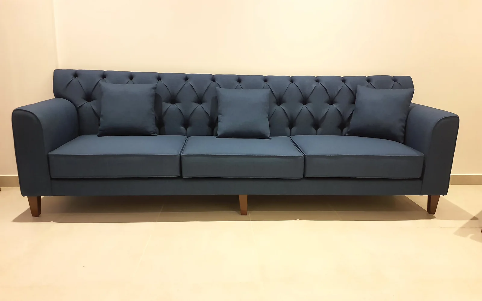 Blue three-seat sofa with a button-tufted back and three cushions.