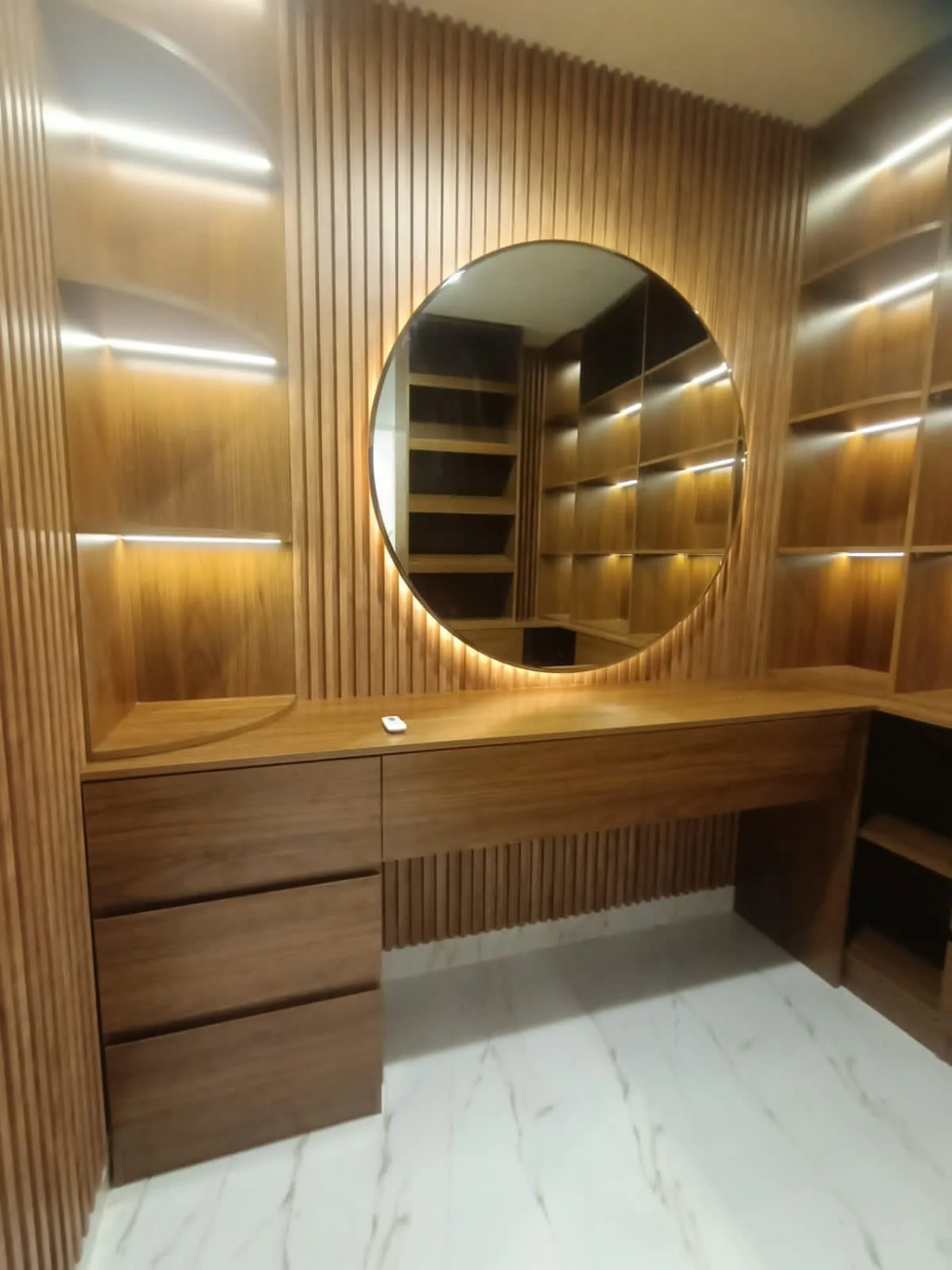 Timber-toned dressing table and round illuminated mirror.