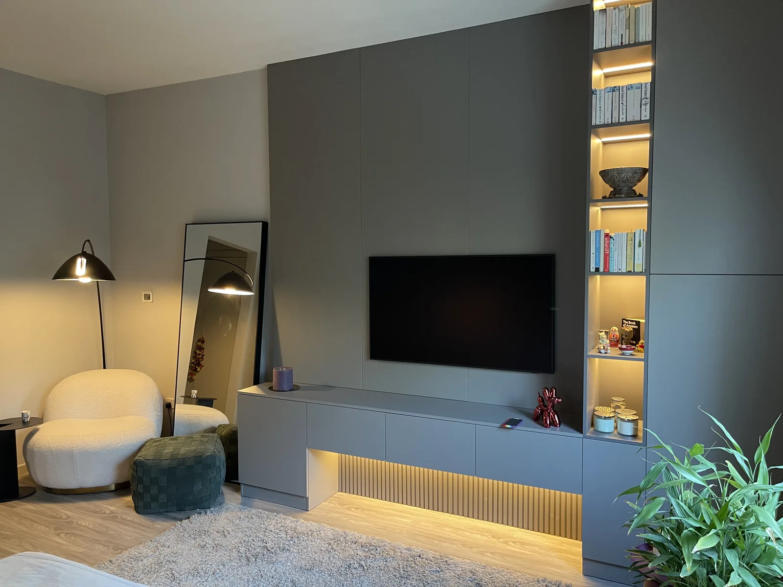 Dark grey media wall with illuminated shelving and reading chair.
