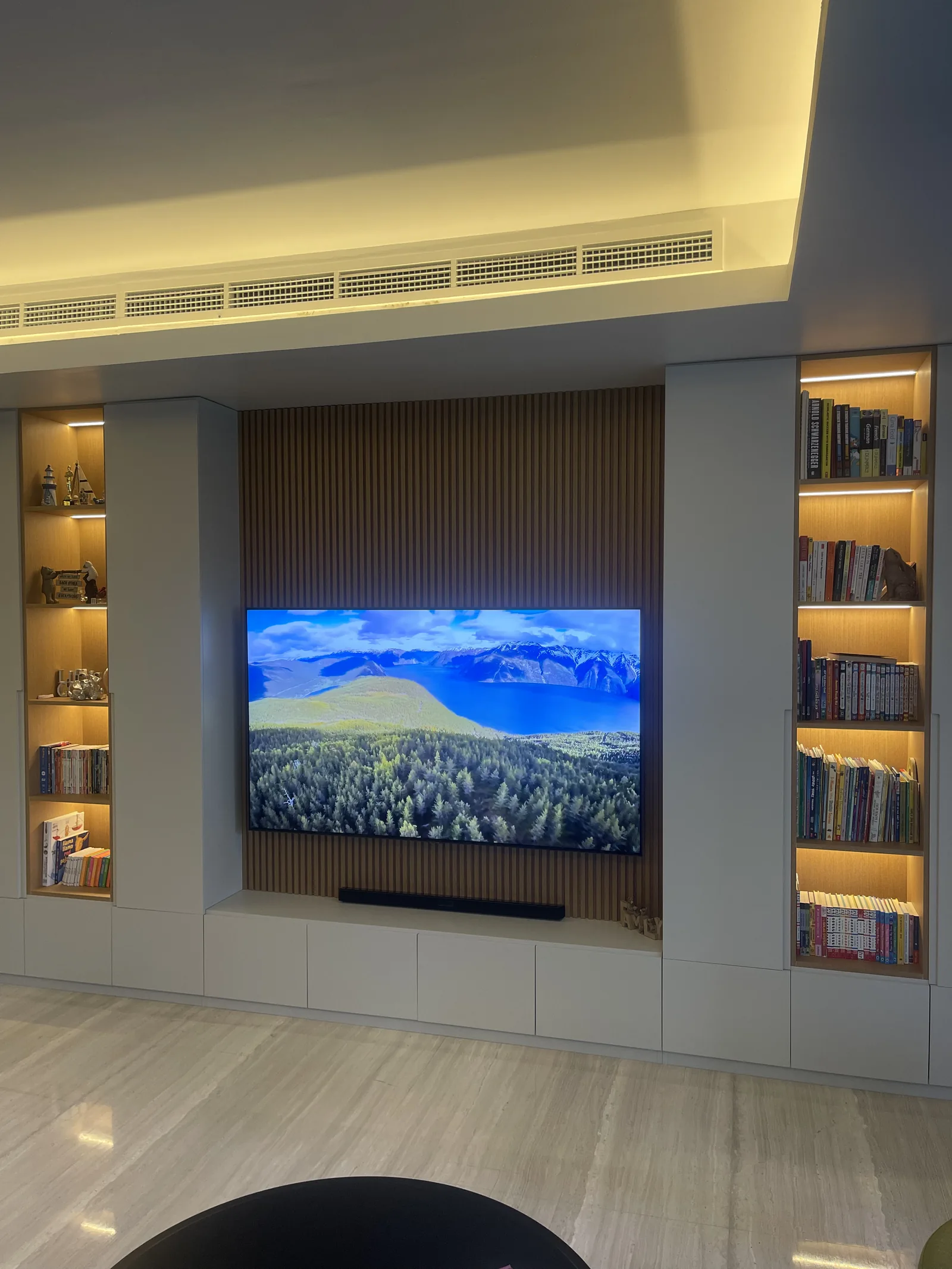 Media wall with fluted timber-toned and illuminated book niches.