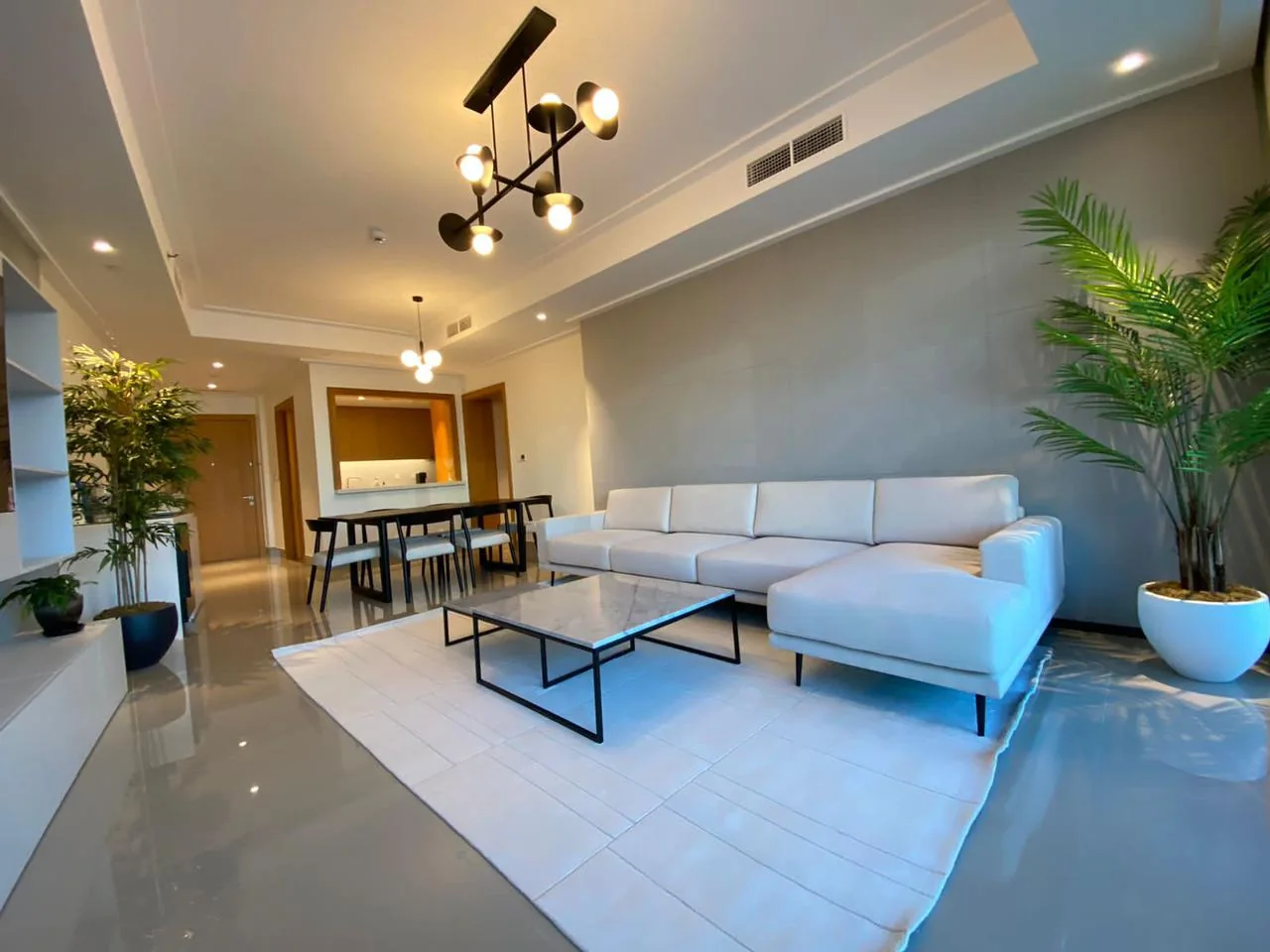 Pale sectional, black-framed coffee tables and dining furniture.