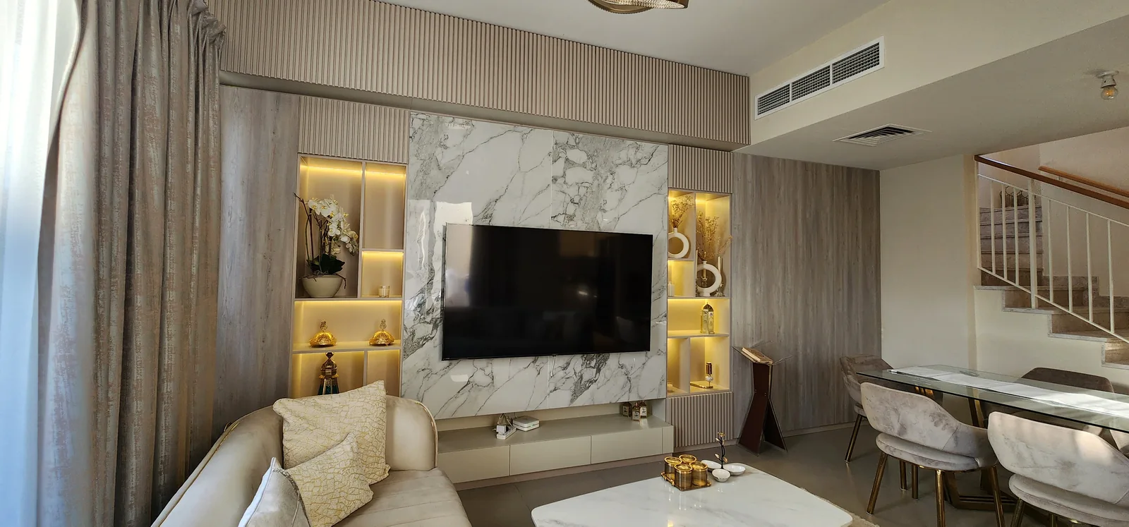 Illuminated veined-panel TV wall, fluted joinery, living and dining setting.