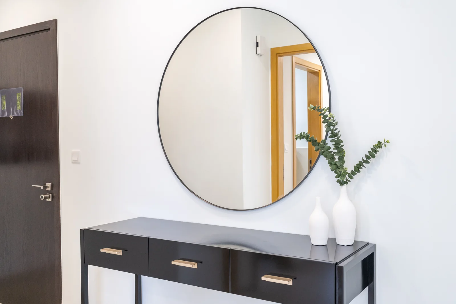 Black three-drawer console with gold-toned pulls below a large round mirror in the entrance.