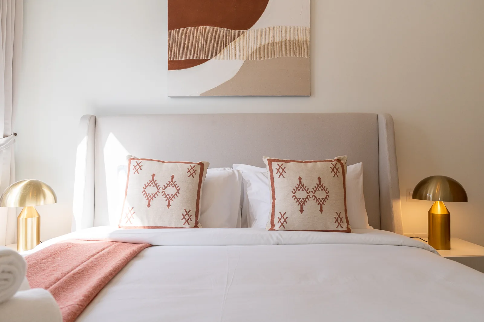Winged upholstered headboard with embroidered cushions and two gold-toned mushroom lamps.