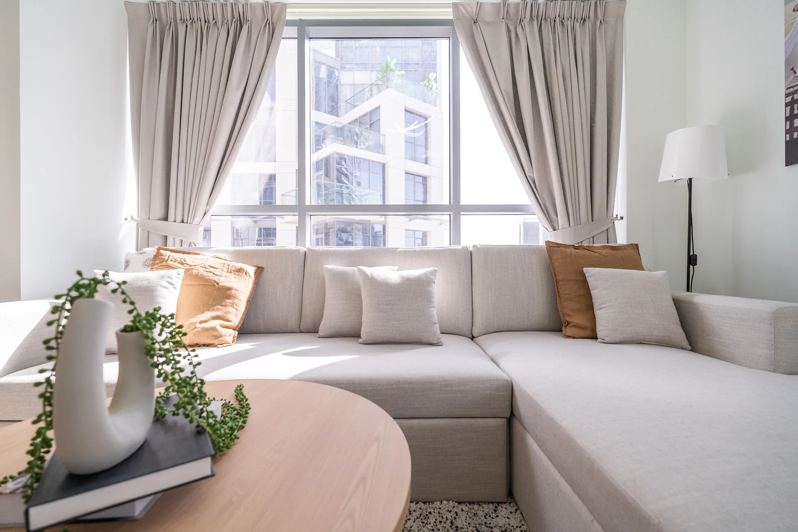 Pale sectional sofa with ochre and ivory cushions in front of a curtained window.