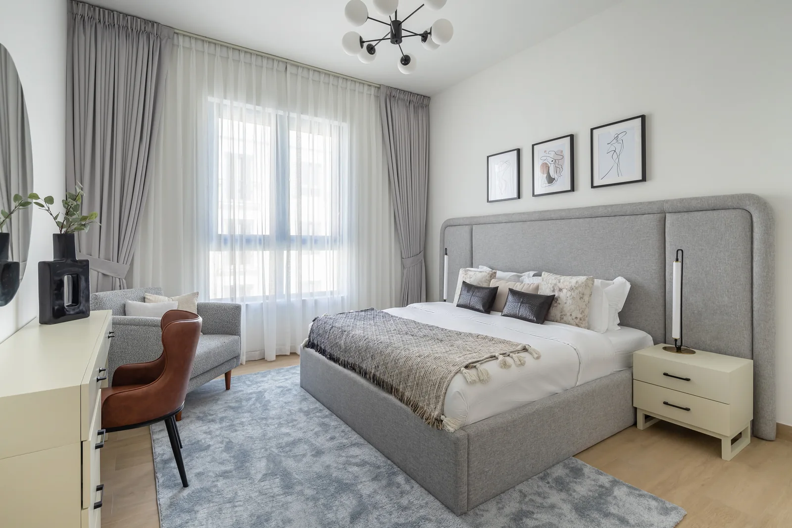 Grey upholstered bed, pale bedside tables and a dressing desk by the window.