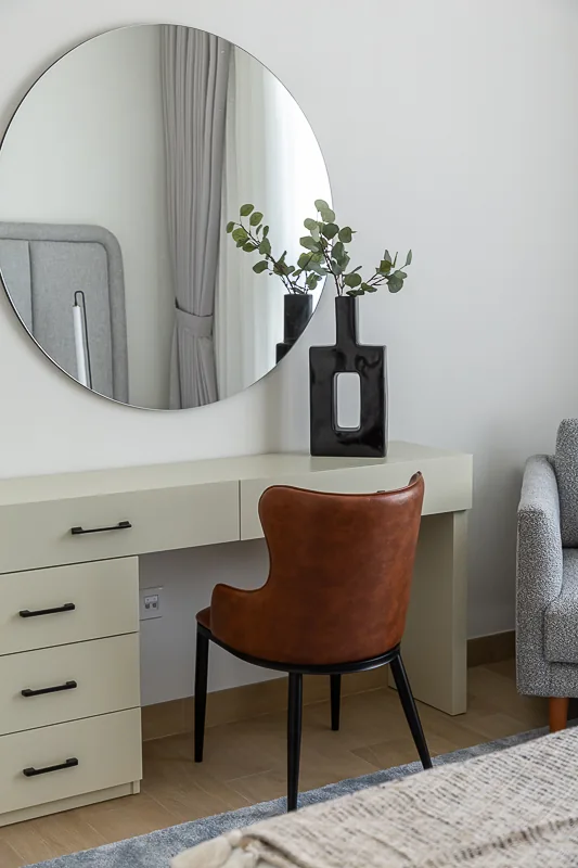 Pale dressing desk, round mirror and rust-coloured chair.