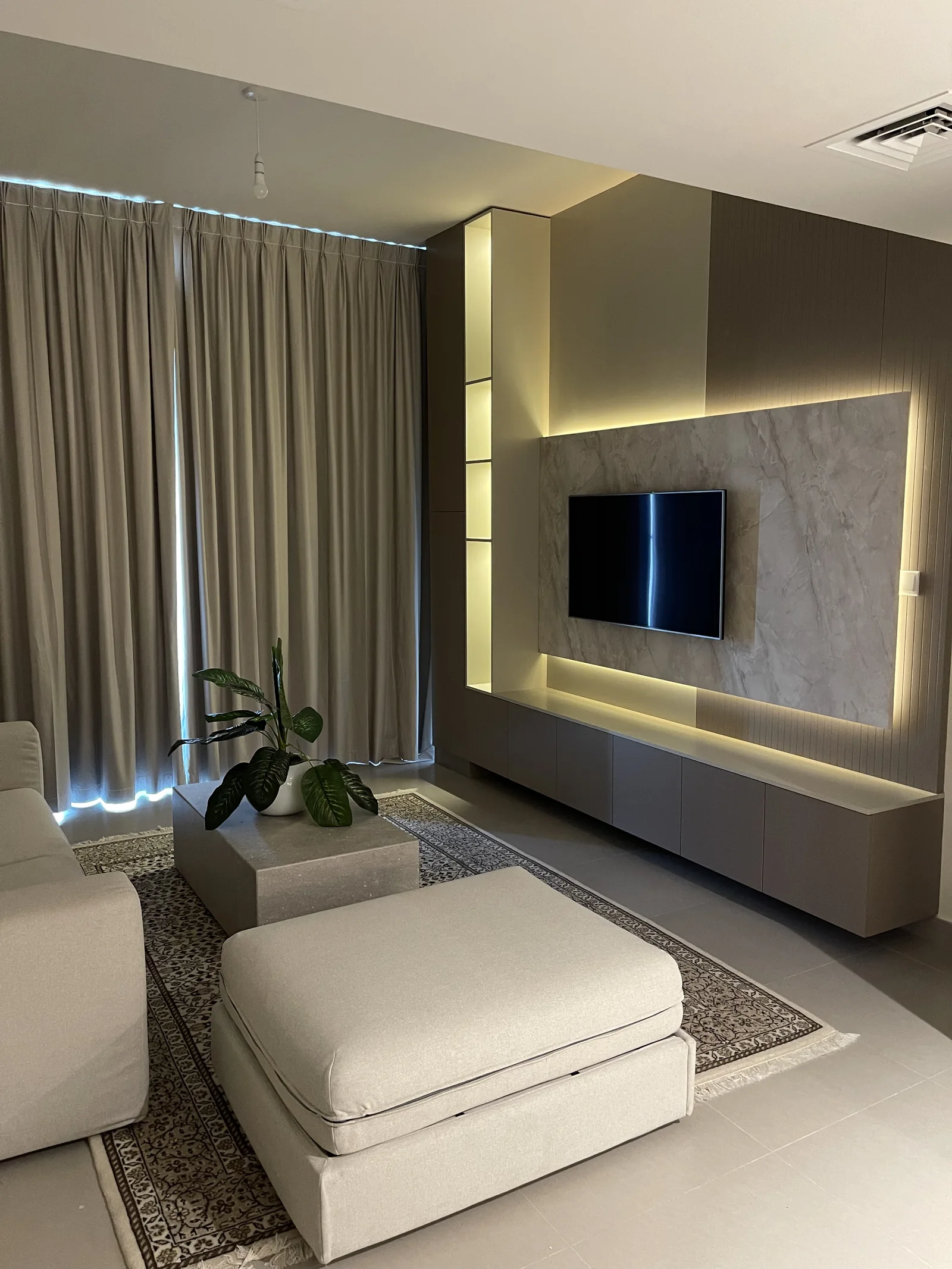 Pale living area with an illuminated veined TV-wall panel and upholstered seating.