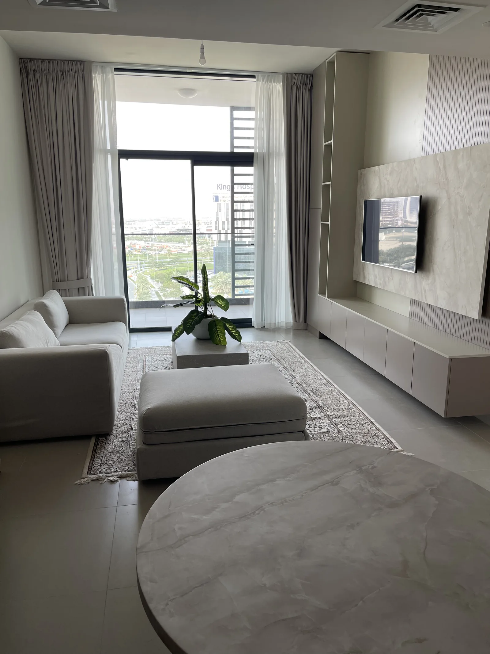 Living room in daylight with the TV wall, pale sectional and a round side table in the foreground.