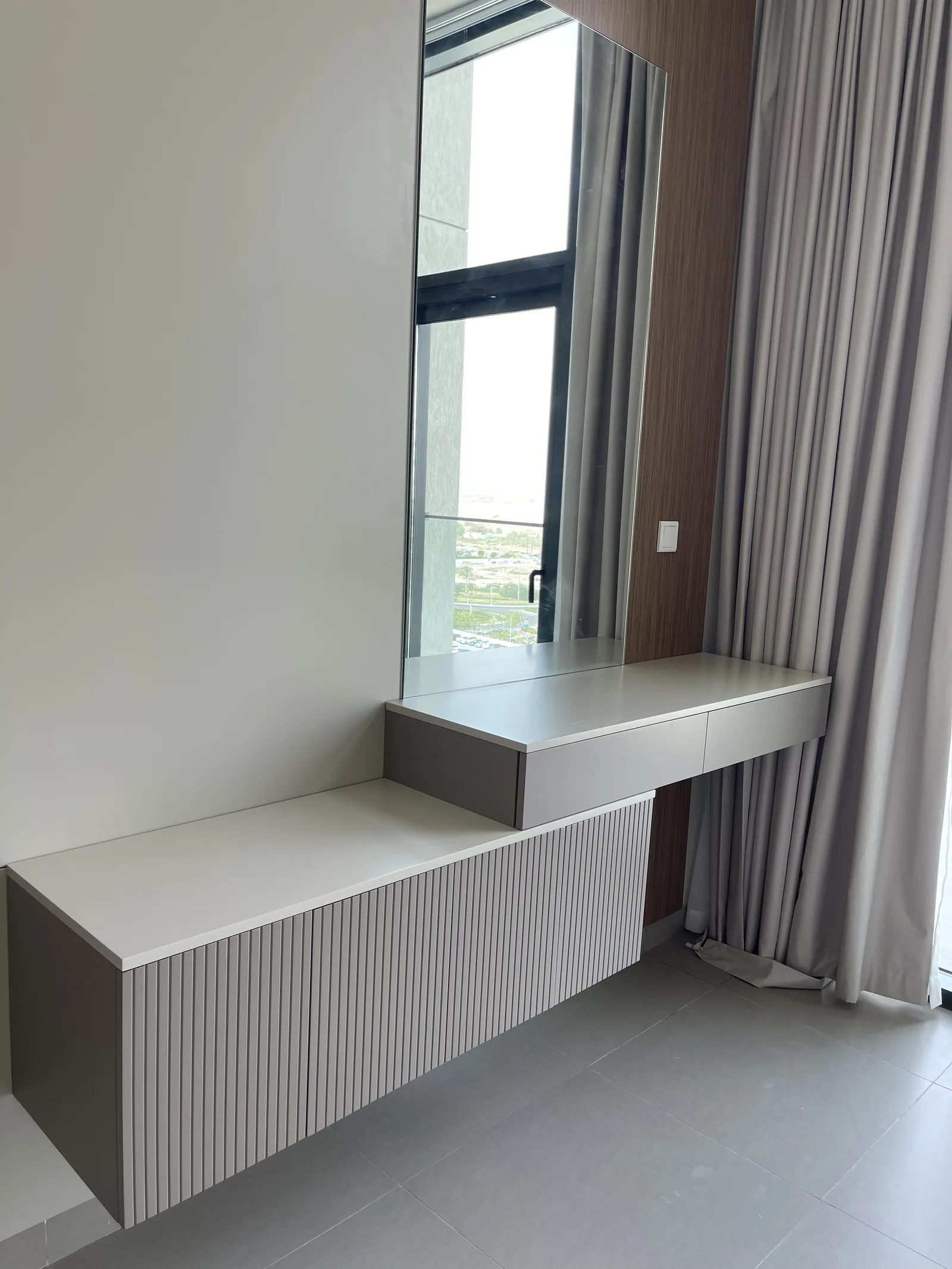 Floating dressing console above a ribbed lower cabinet, beside a tall mirror and window.