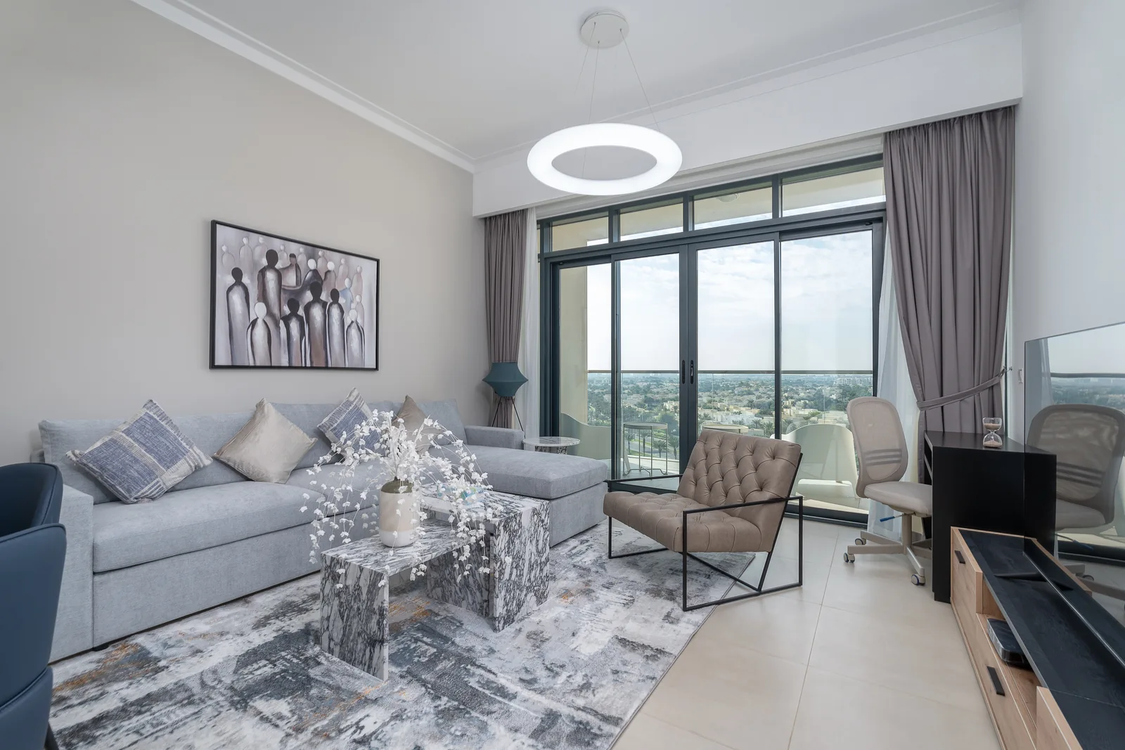 Grey sectional, upholstered chair and patterned tables beside a tall window.