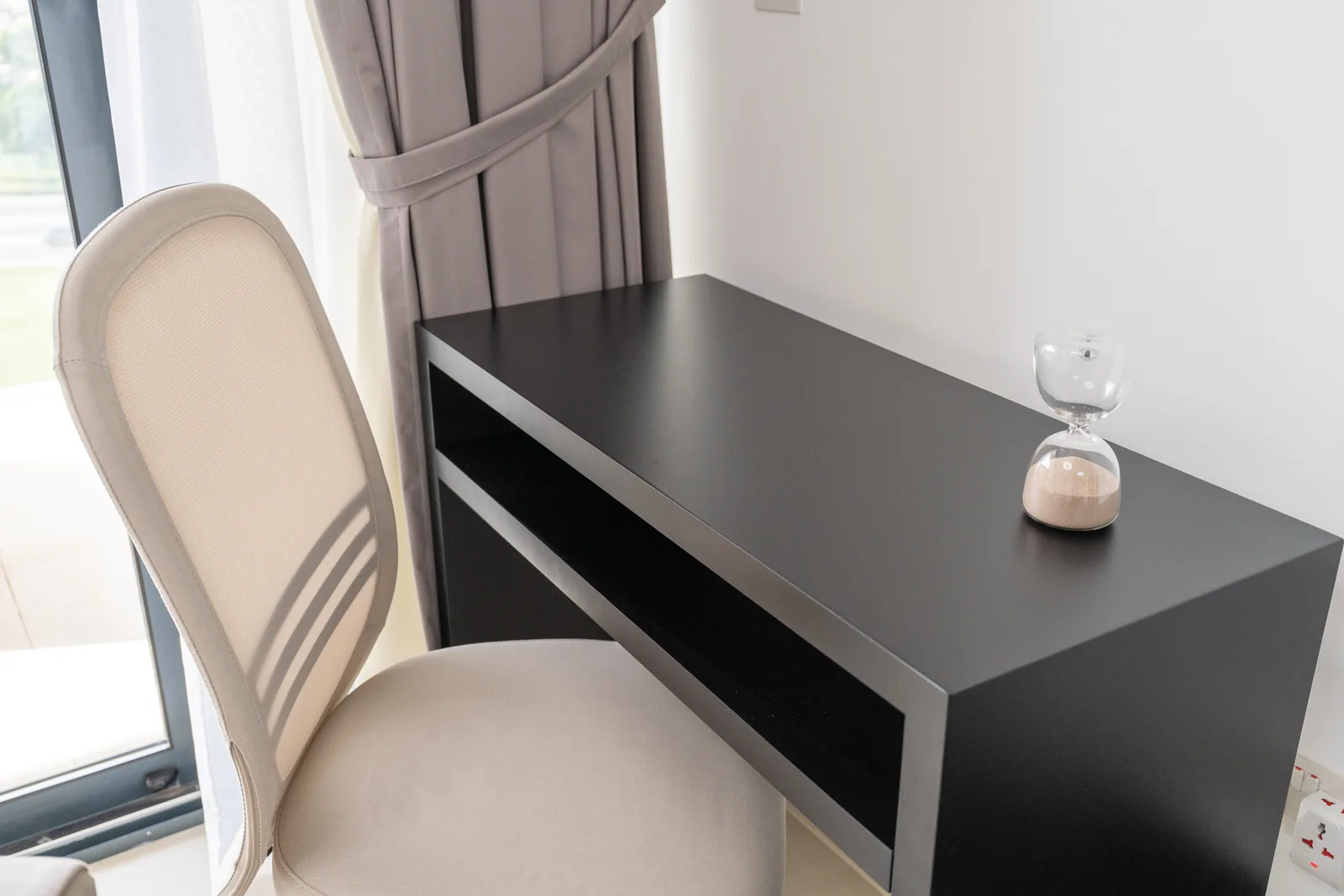 Compact black desk, cream office chair and hourglass.