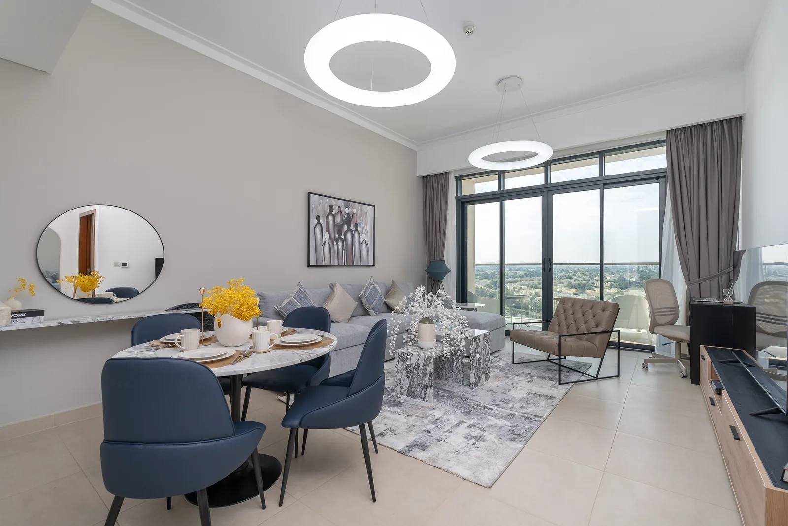 Open-plan living and dining with grey sectional, blue dining chairs and patterned tables.