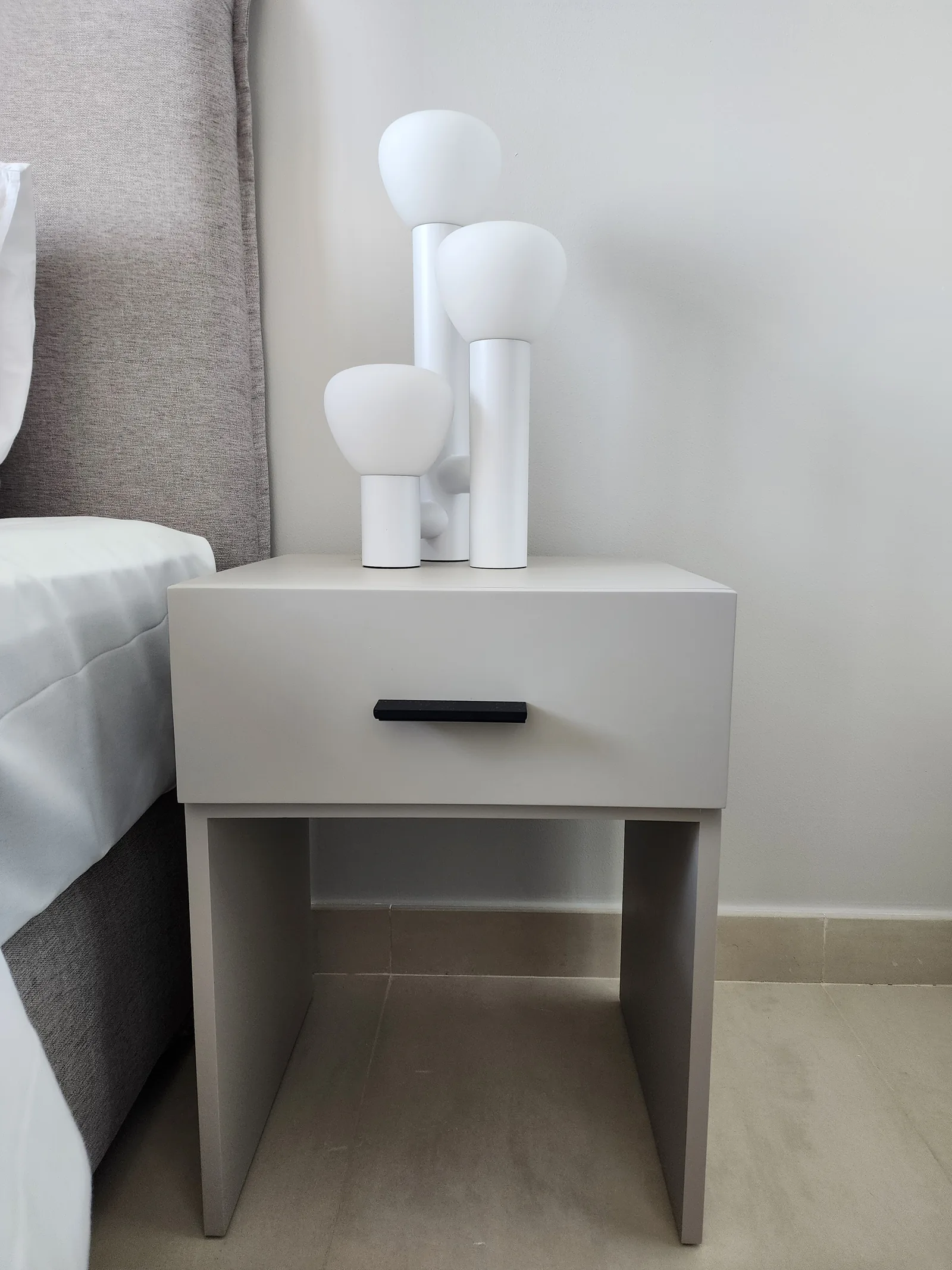 Bedside table and white sculptural three-light lamp.