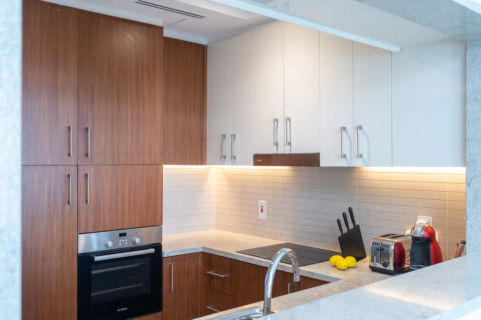 Kitchen cabinetry and illuminated backsplash seen through the pass-through.