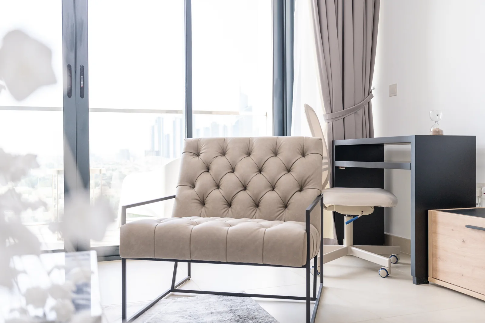 Tufted lounge chair on black metal-toned frame beside window.
