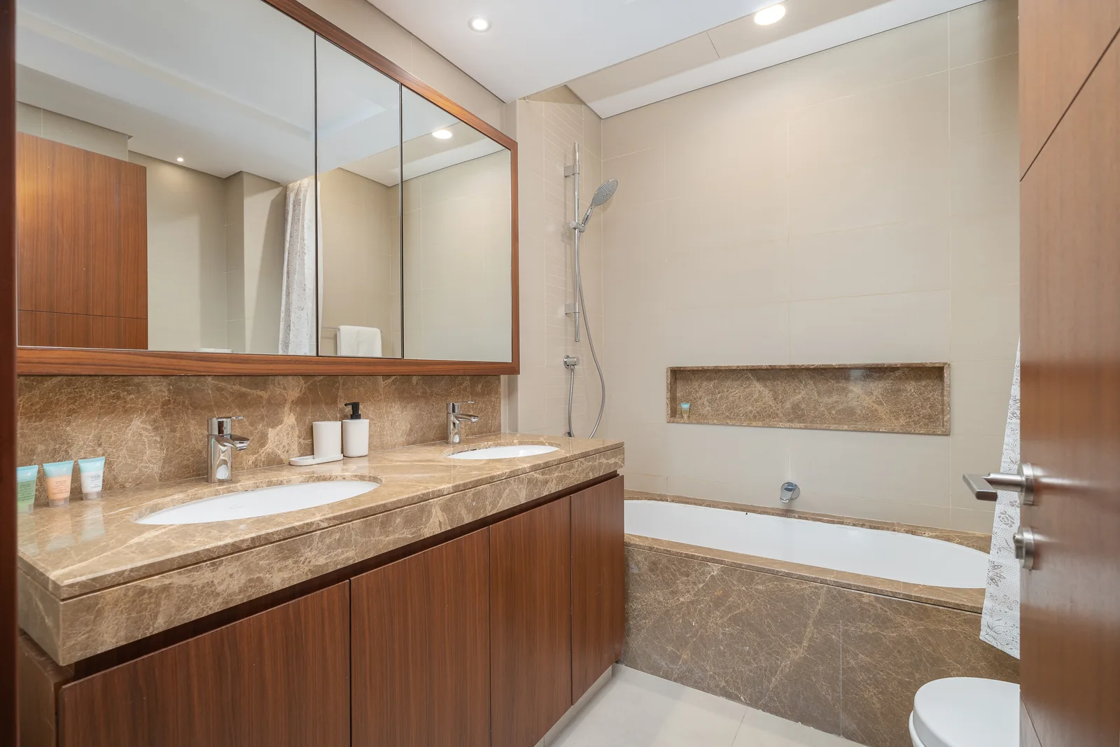 Double vanity and bathtub with warm brown surfaces.