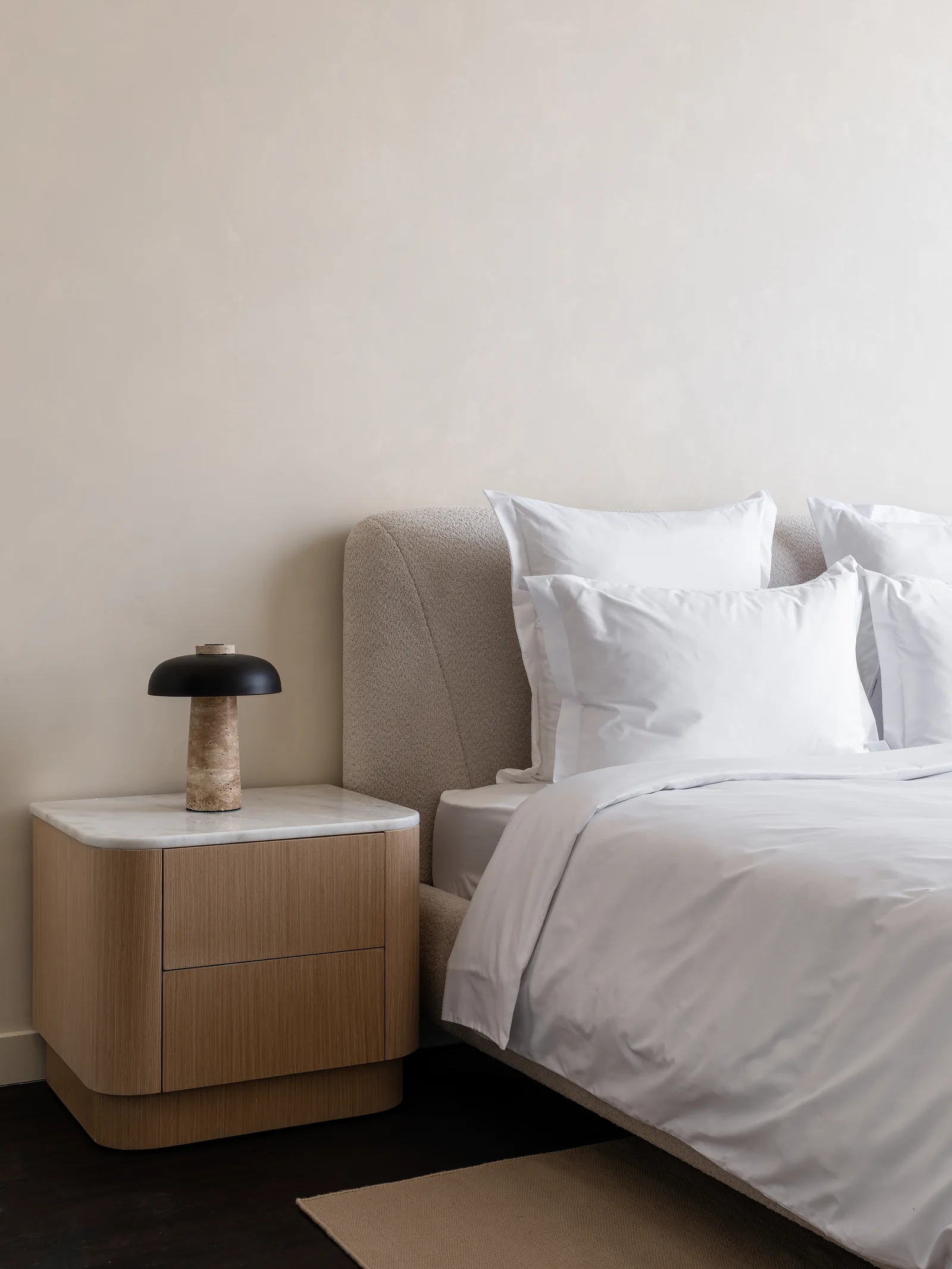 Rounded bedside cabinet, lamp and upholstered headboard.