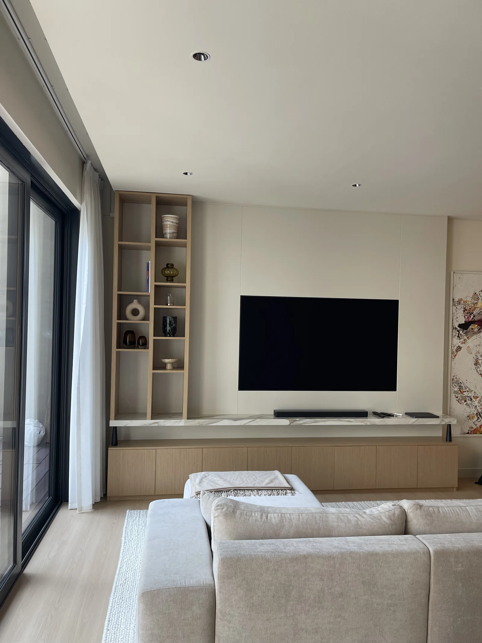 Television and low timber-toned cabinetry with tall open shelves beside a window.