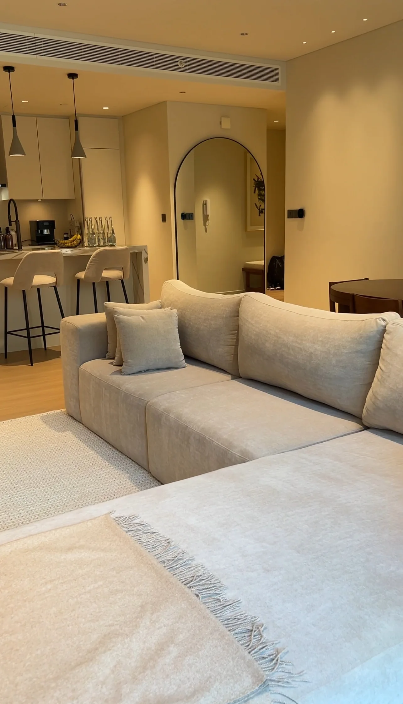 Pale sectional sofa with the open kitchen and an arched mirror behind.