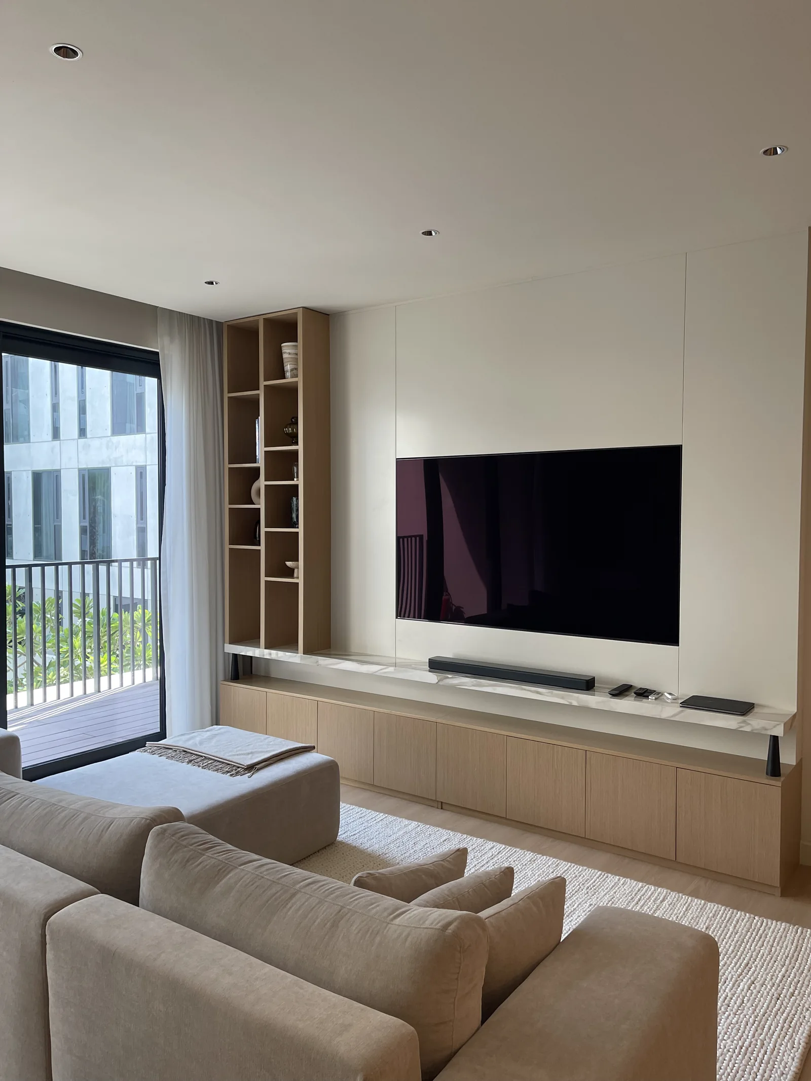Angled view of the low media cabinet, display shelves and pale sofa by the window.