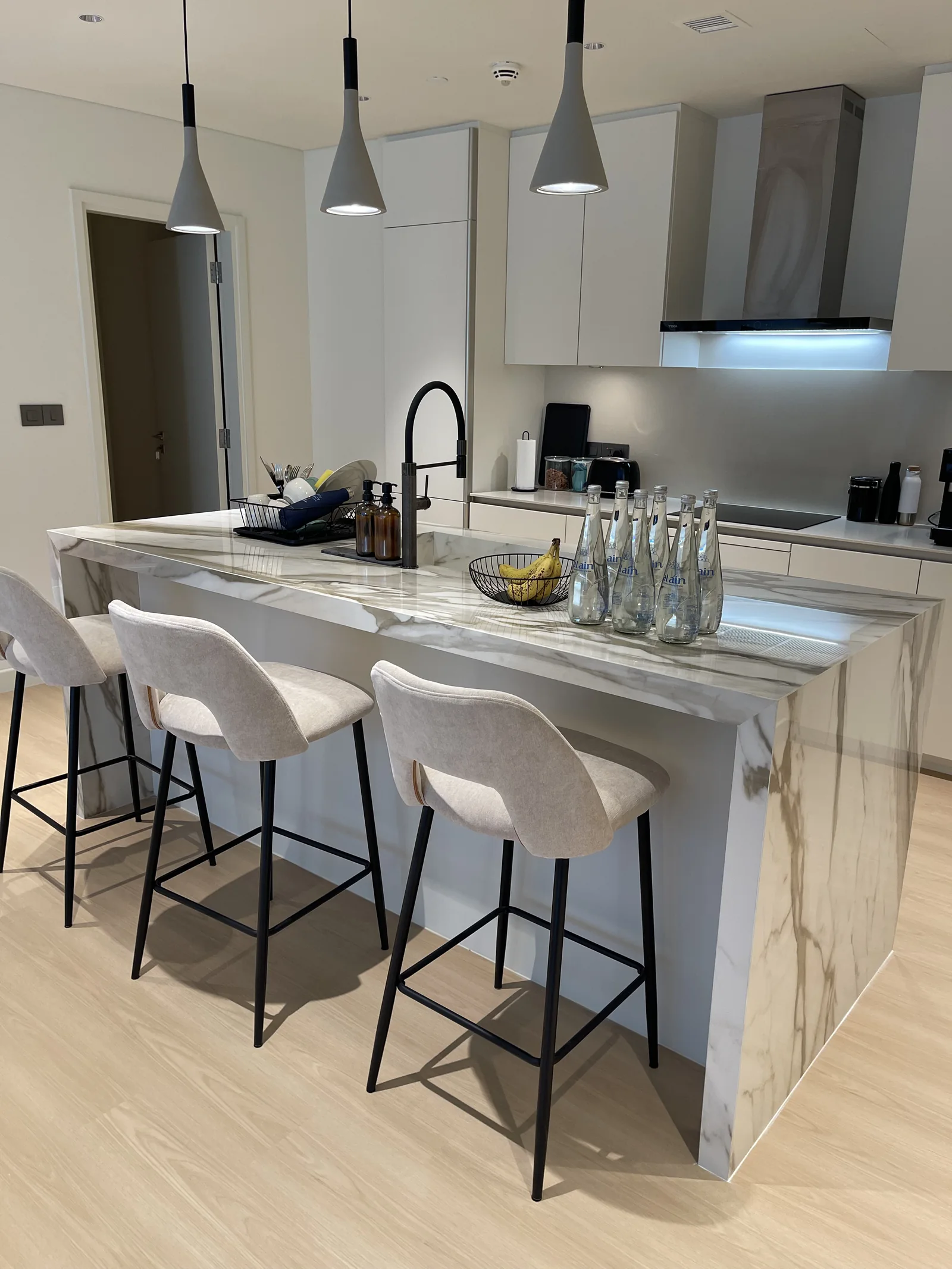 Veined kitchen island with pale upholstered stools under pendant lights.