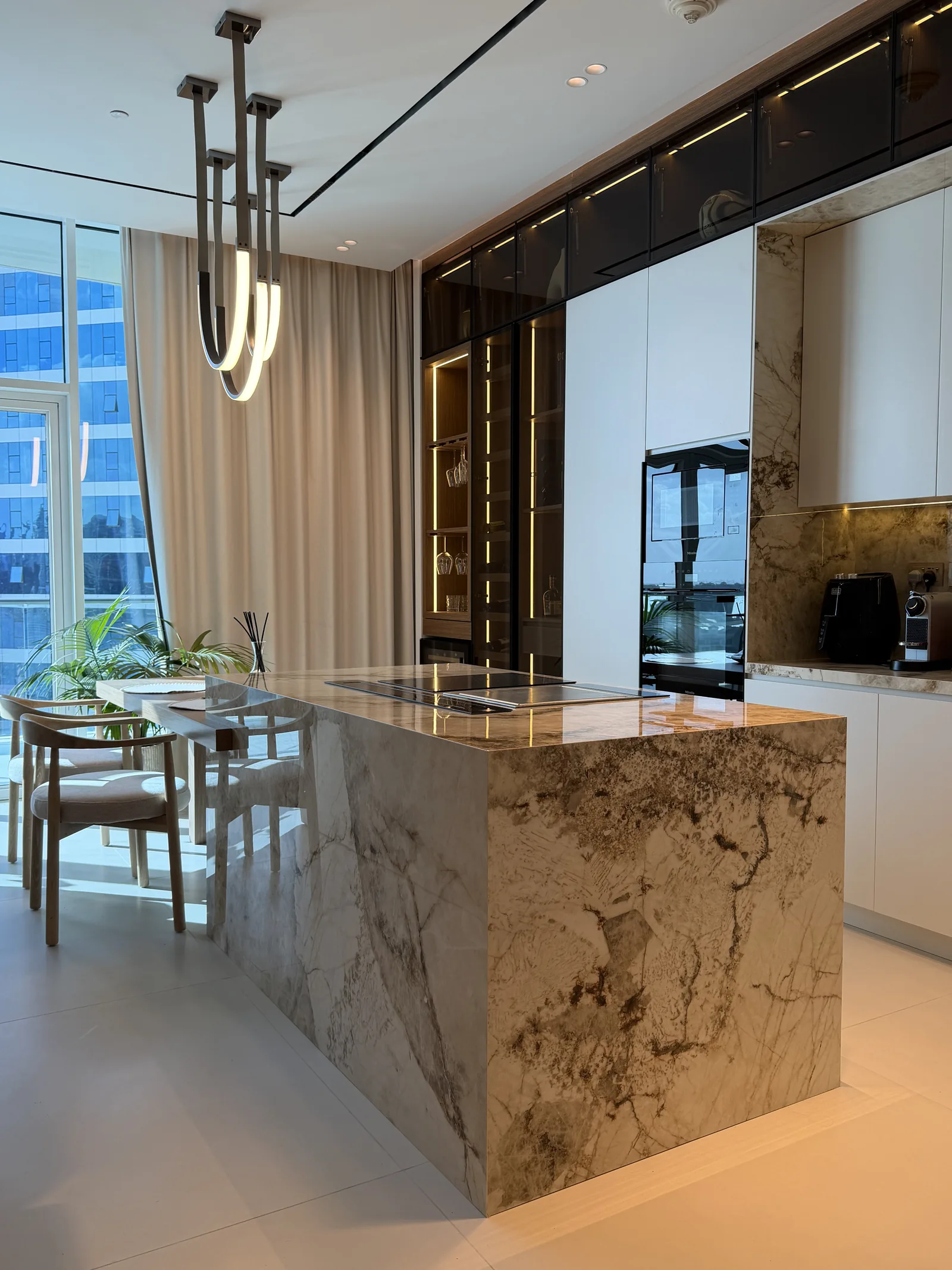 Kitchen island with a veined surface, timber-toned panels and dark glazed upper cabinets.