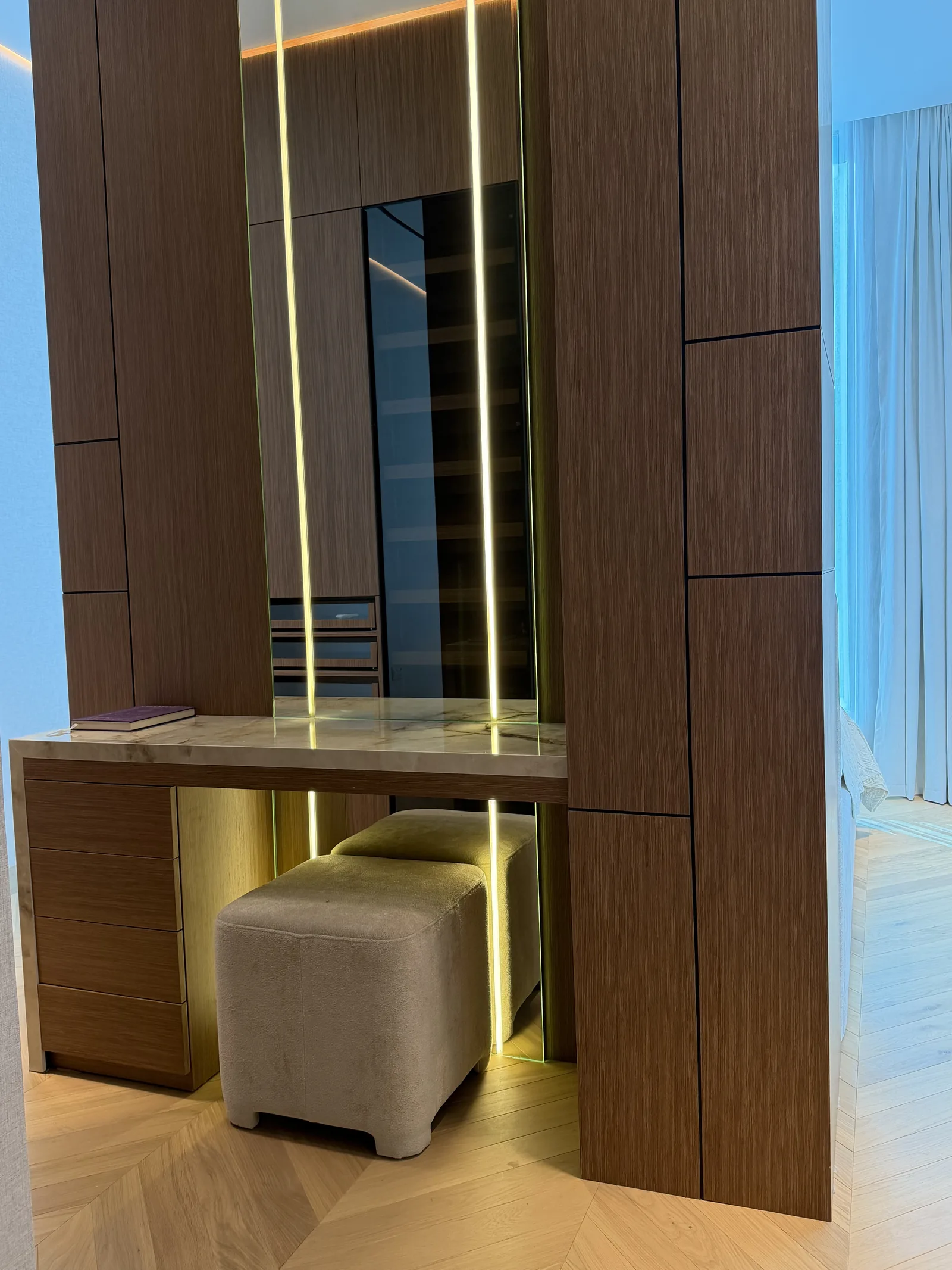 Timber-toned dressing area with an illuminated mirror and upholstered stool.