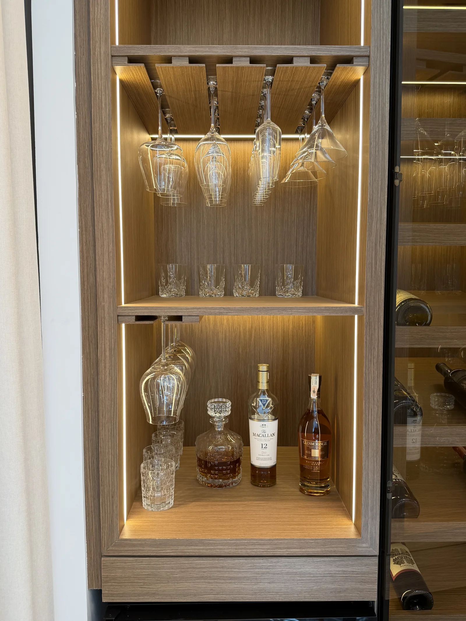 Illuminated timber-toned bar compartment and hanging-stemware storage.