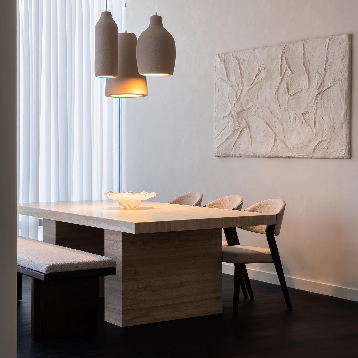 Travertine dining table, timber chairs and a solid wood bench beneath sculptural pendants and a handmade wall mural at Burj Khalifa Residences.