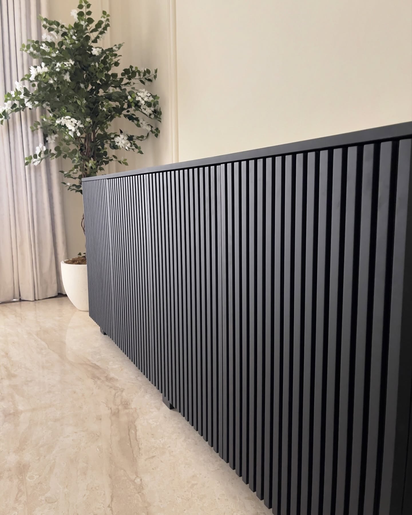Close-up of a dark slatted hallway console beside curtains and a planter.