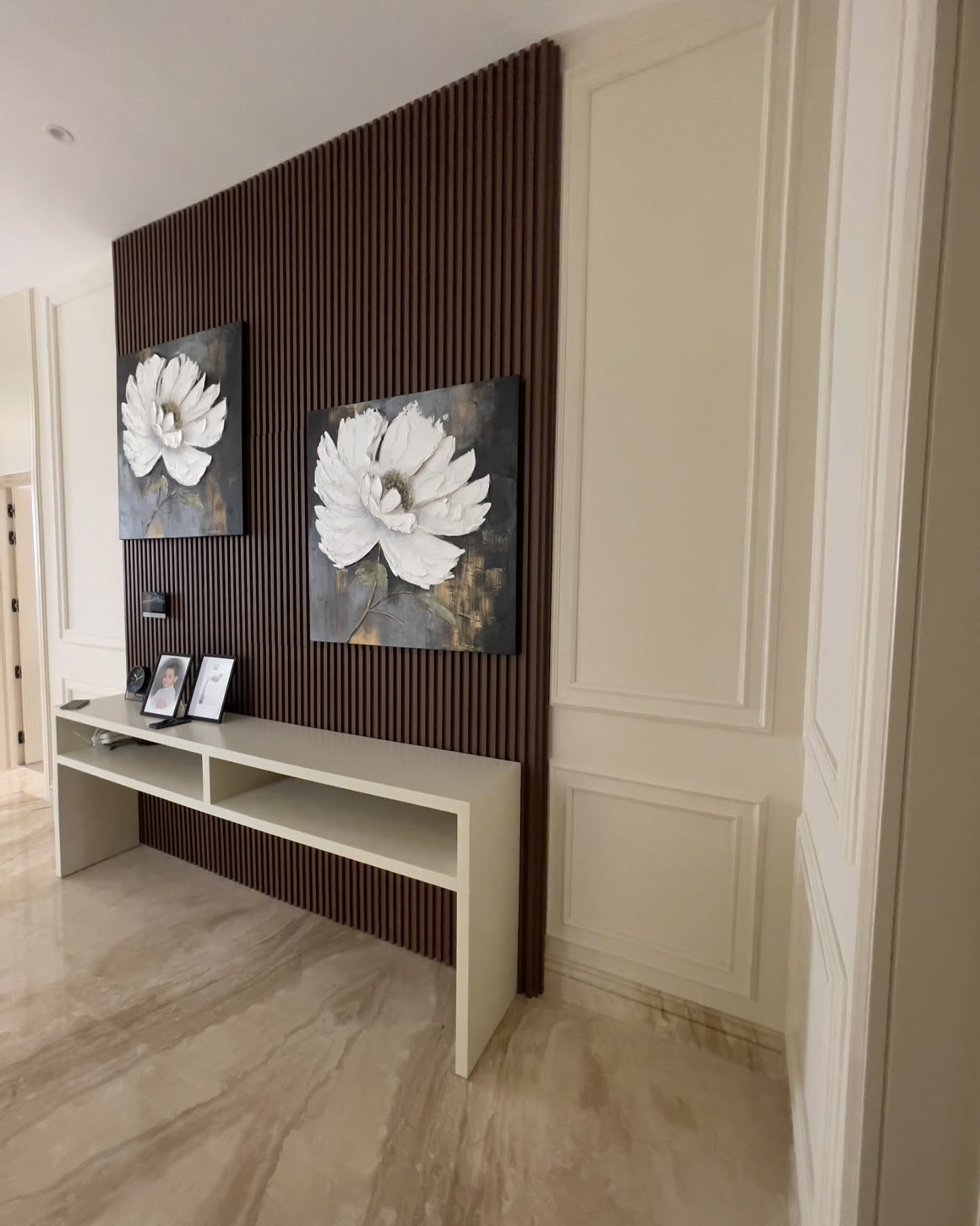 Pale open console table against dark timber slats, wall moulding and floral artwork.