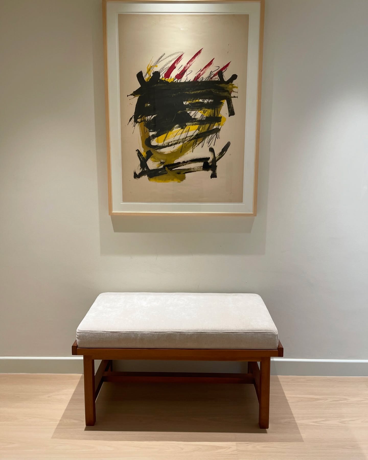 Timber-framed upholstered hallway bench beneath abstract artwork.