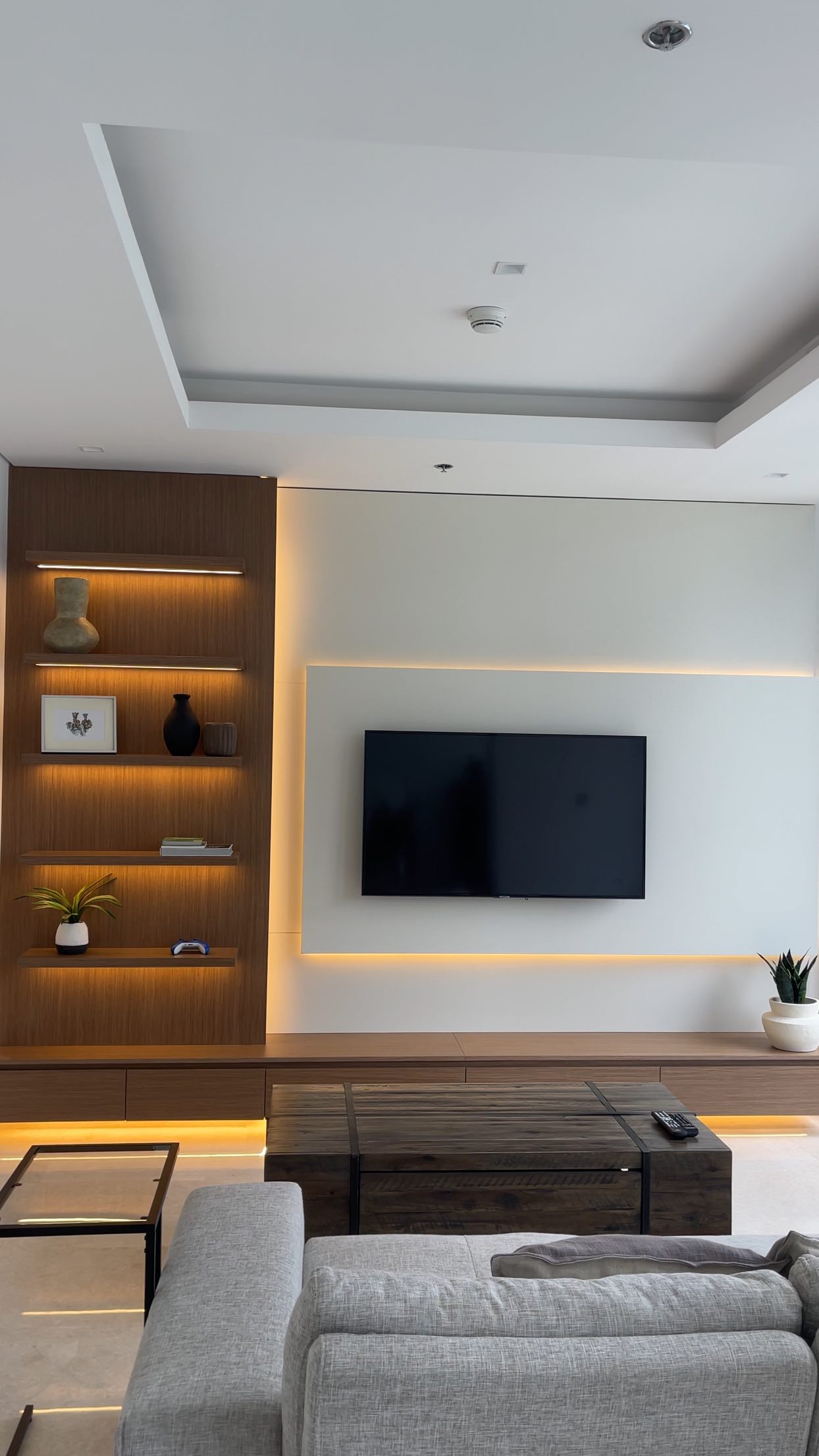 Custom TV wall with warm timber shelving, a pale television panel and concealed LED lighting.